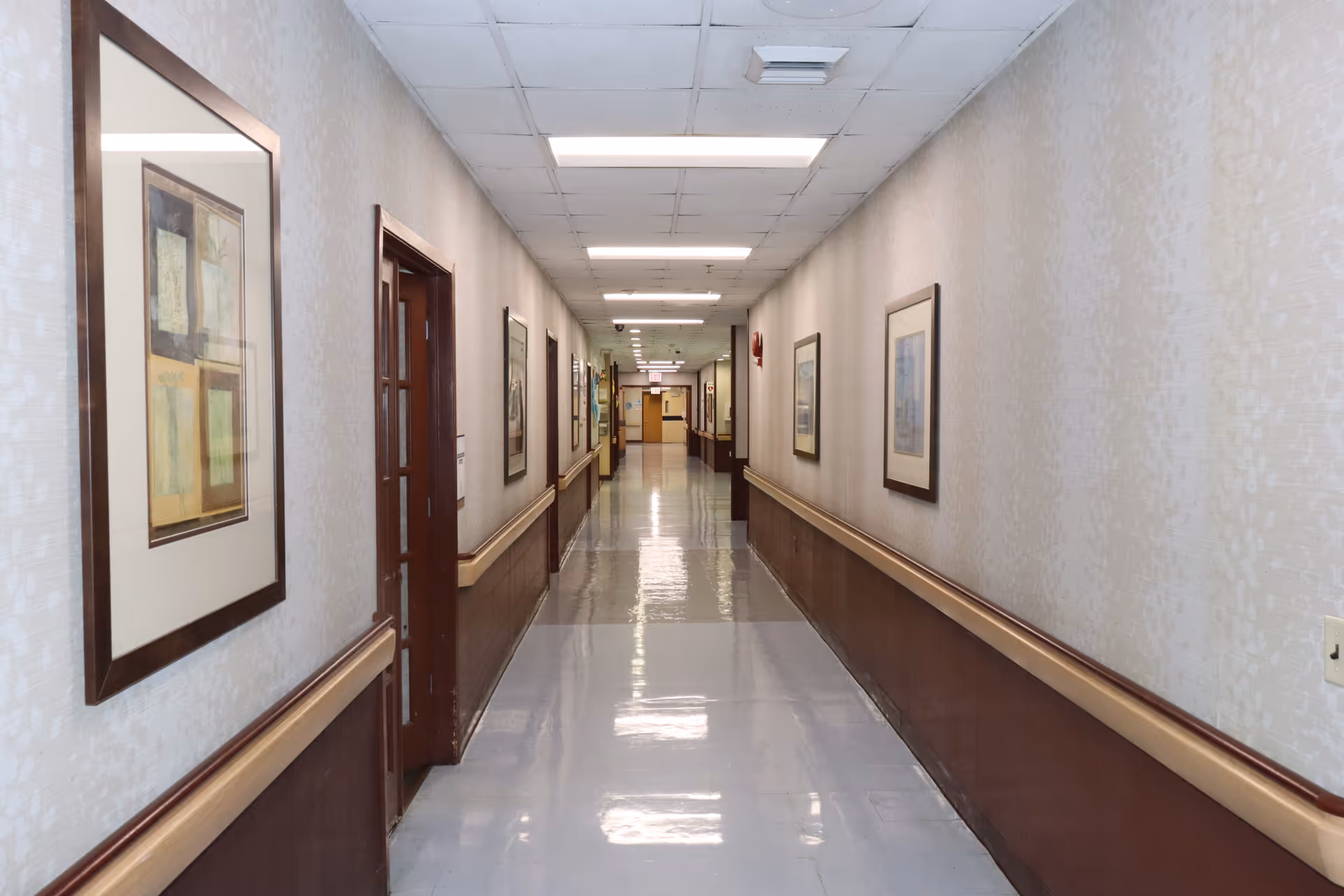 Long hallway in a senior living facility with framed artwork along walls.