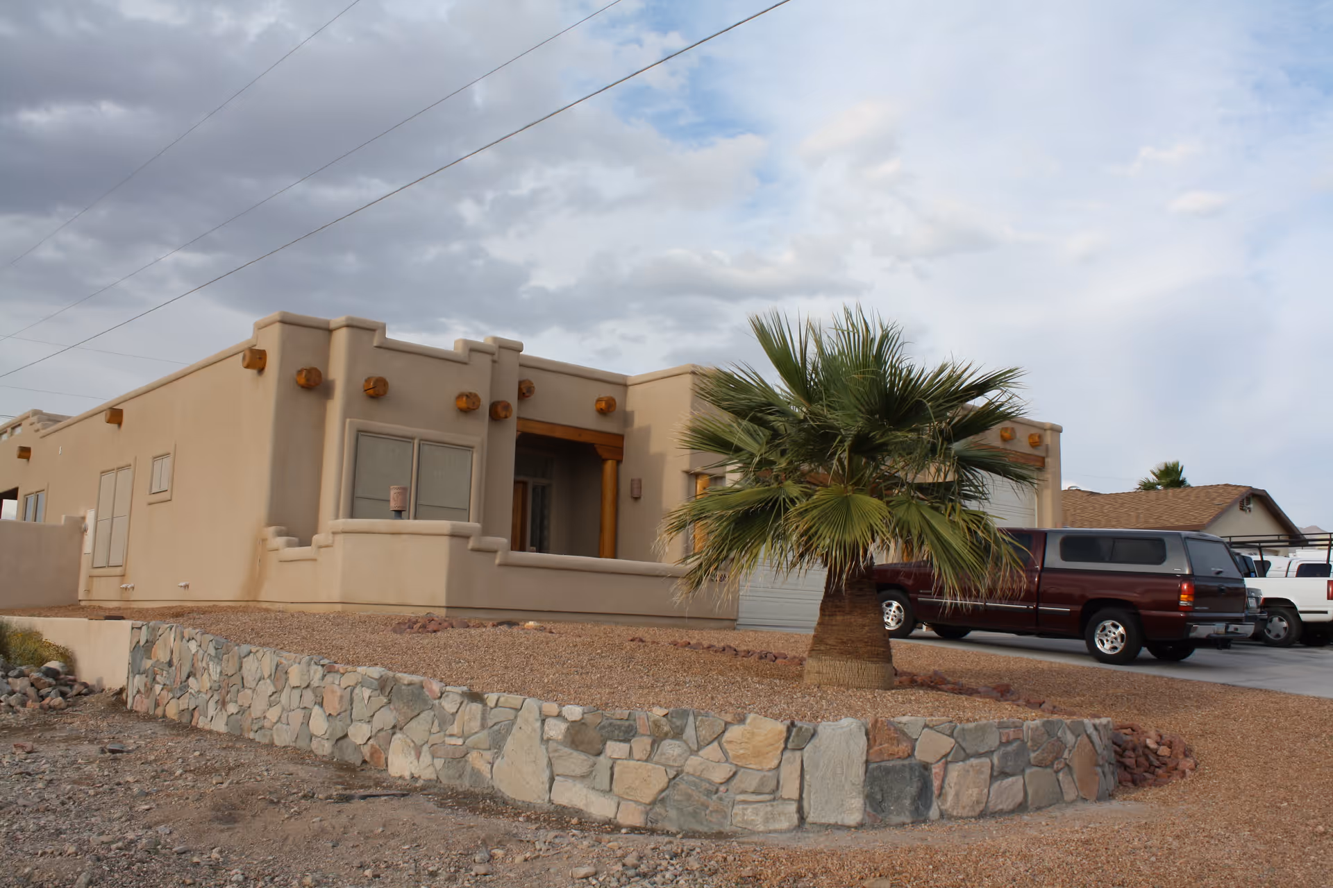 Desert-style senior living facility front exterior with palm tree and parked cars.