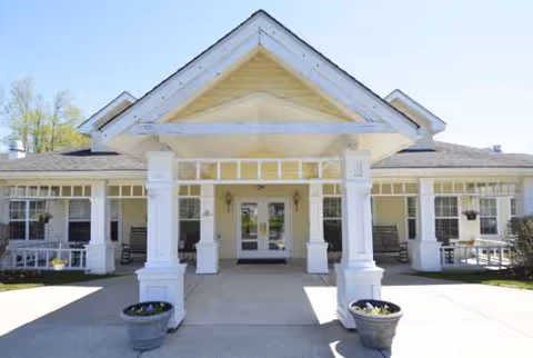 Entrance of a white senior living facility with columns and a shaded walkway.