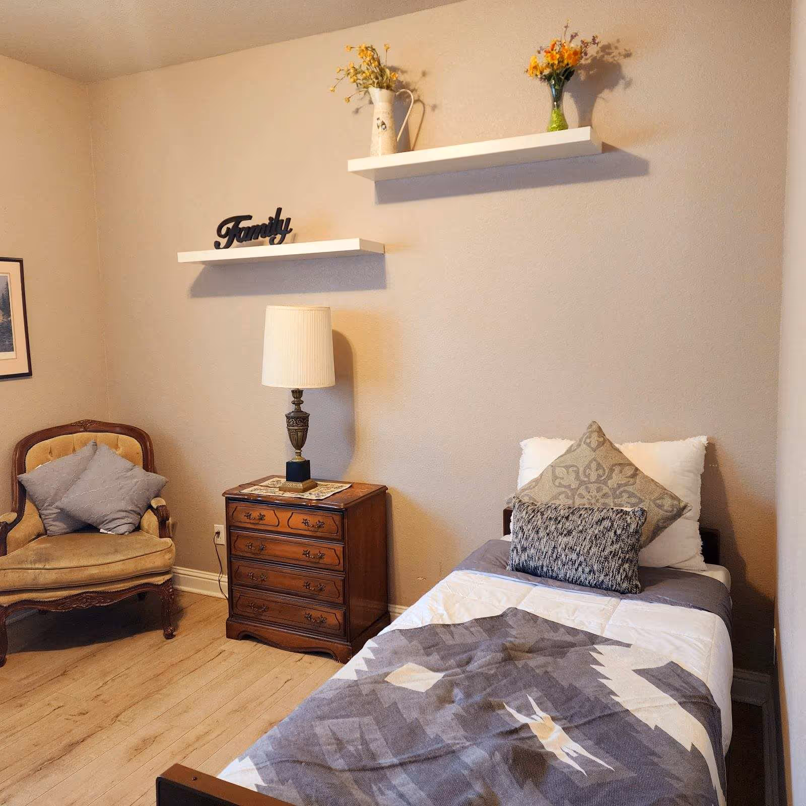 Cozy bedroom with single bed, nightstand, lamp, and decorative wall shelves.