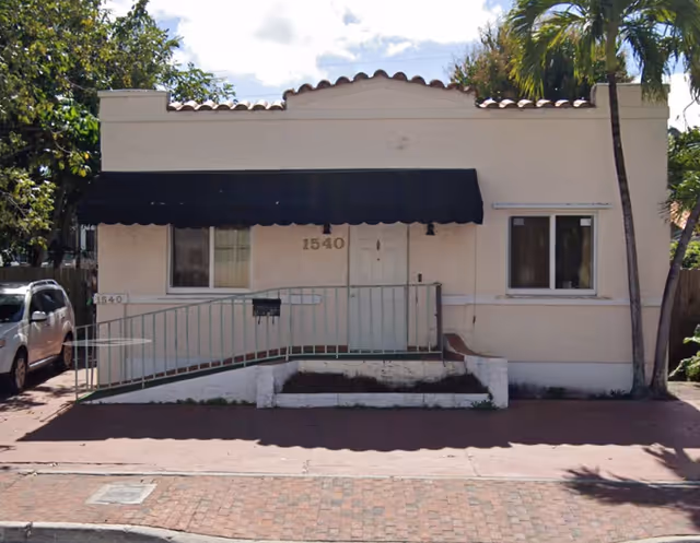 Front exterior of a small beige building with a black awning and ramp.