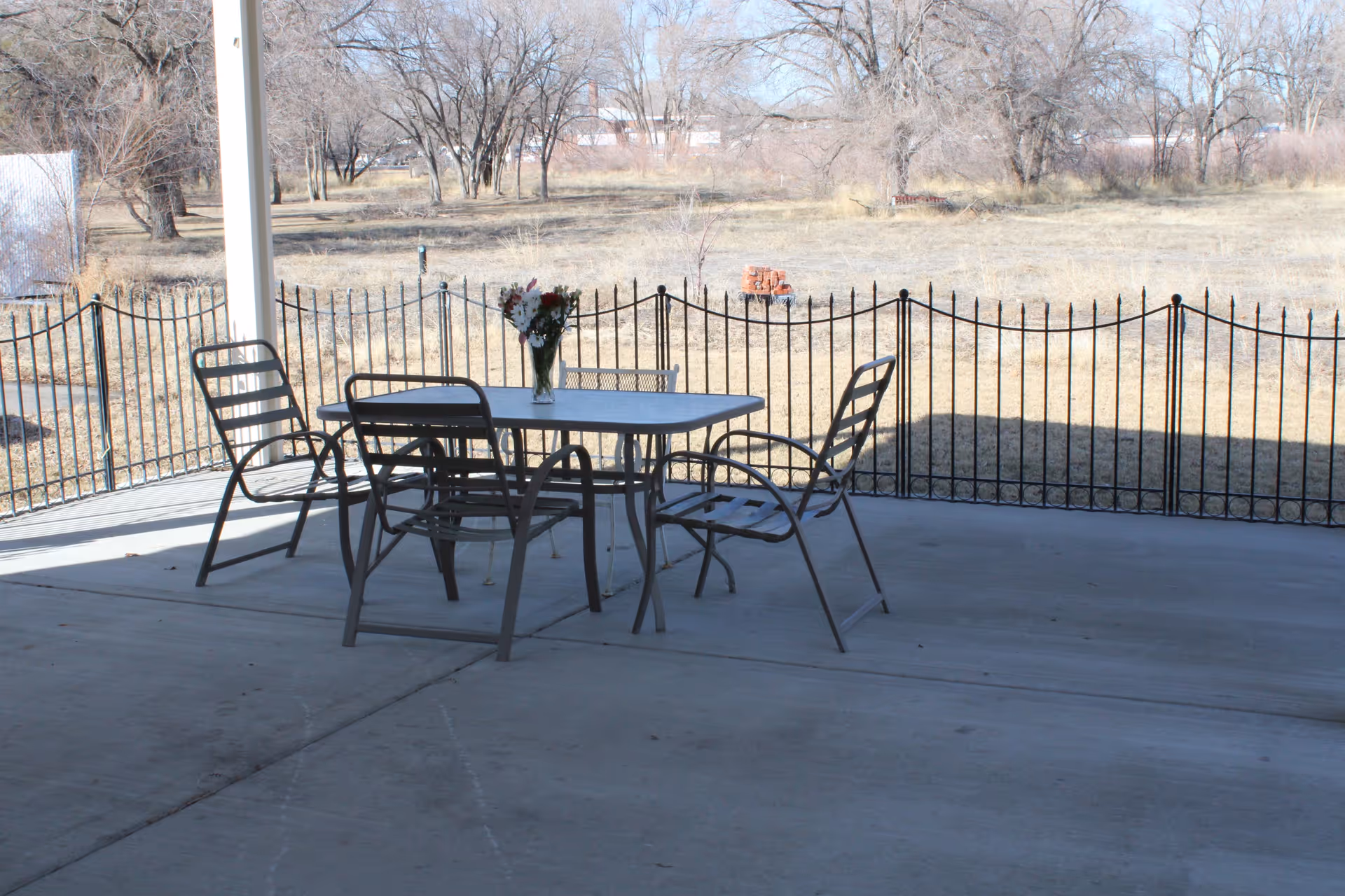 Outdoor patio with metal table and chairs on concrete, vase of flowers