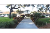 Concrete walkway leads to a single-story Sunshine Christian Homes entrance with green lawn and palm trees.