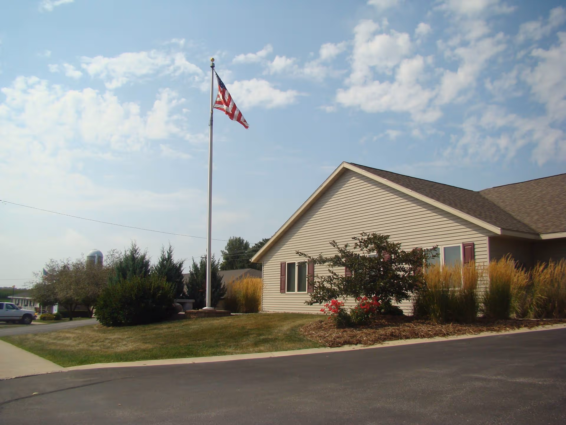 Single-story beige senior living facility exterior with a tall flagpole and landscaped front yard.