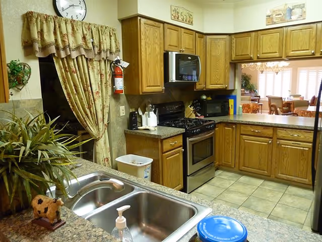 Aladdin Assisted Living kitchen with wooden cabinets, stainless appliances, and a pass-through to dining area.