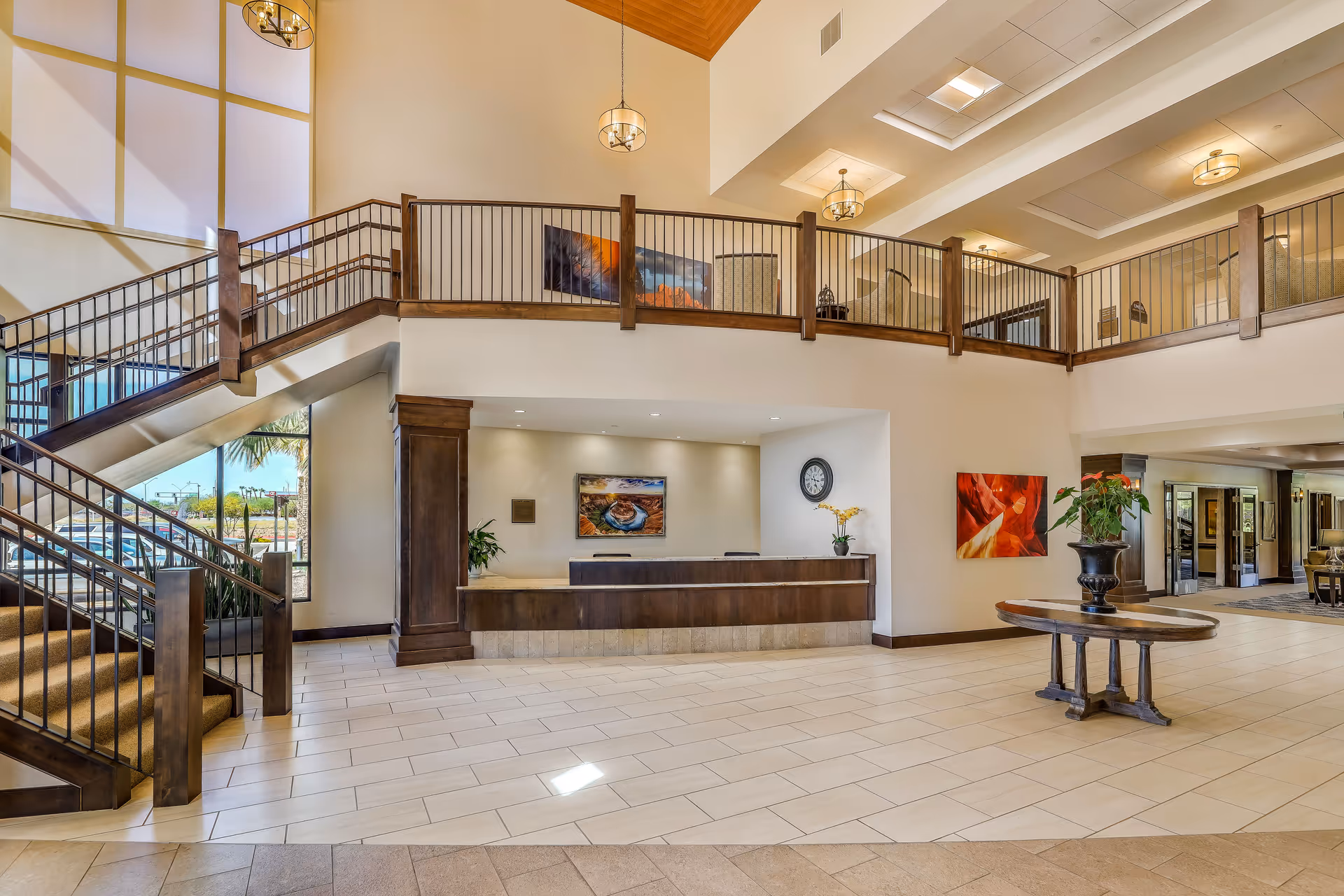 Bright lobby with a reception desk, staircase, and upper balcony in a senior living facility.