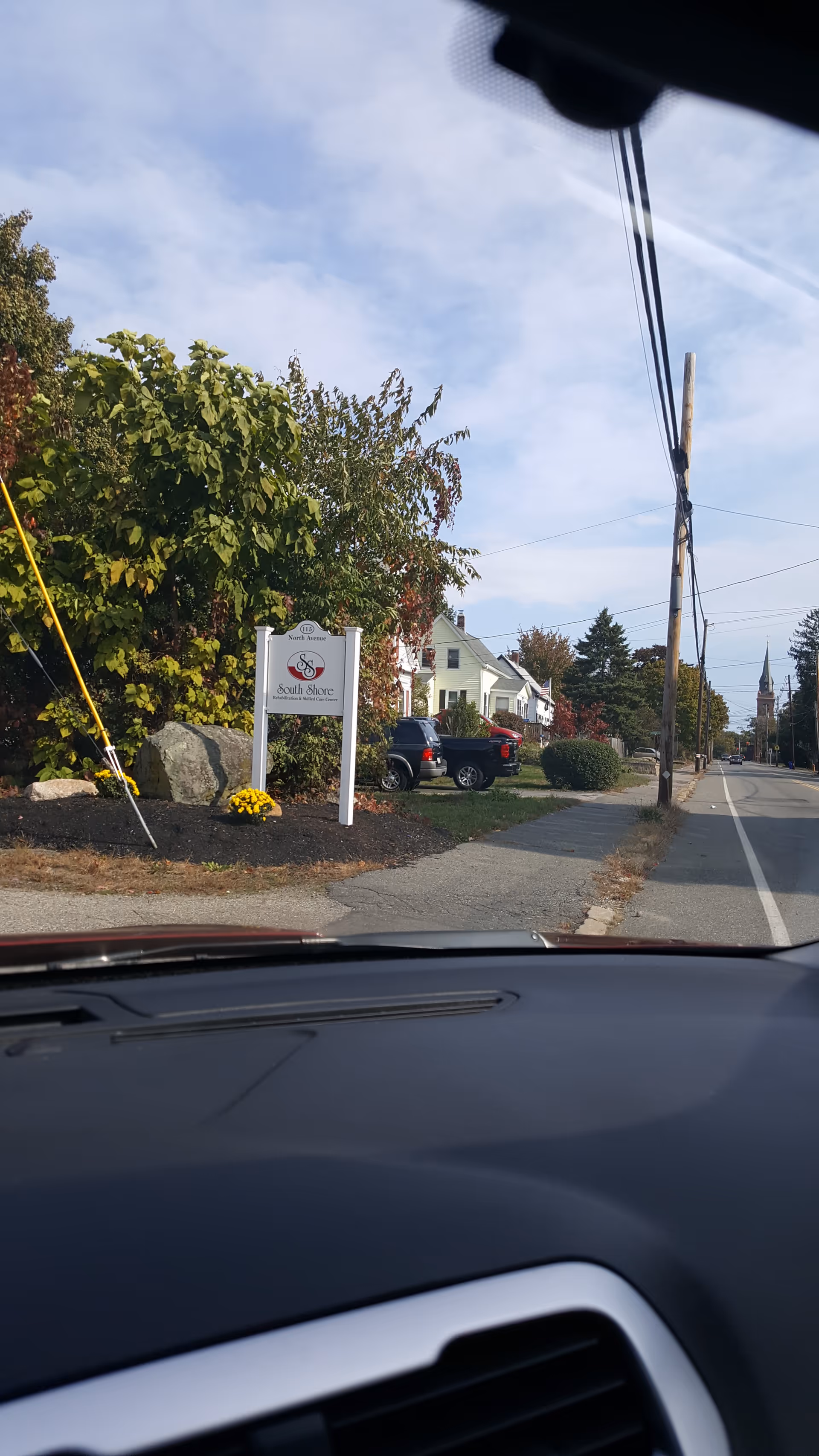 Street view with South Shore Rehabilitation and Skilled Care Center sign, trees, cars, and houses.