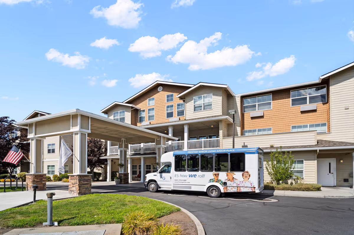 Exterior view of Prestige Senior Living Arbor Place with a bus parked at the entrance.