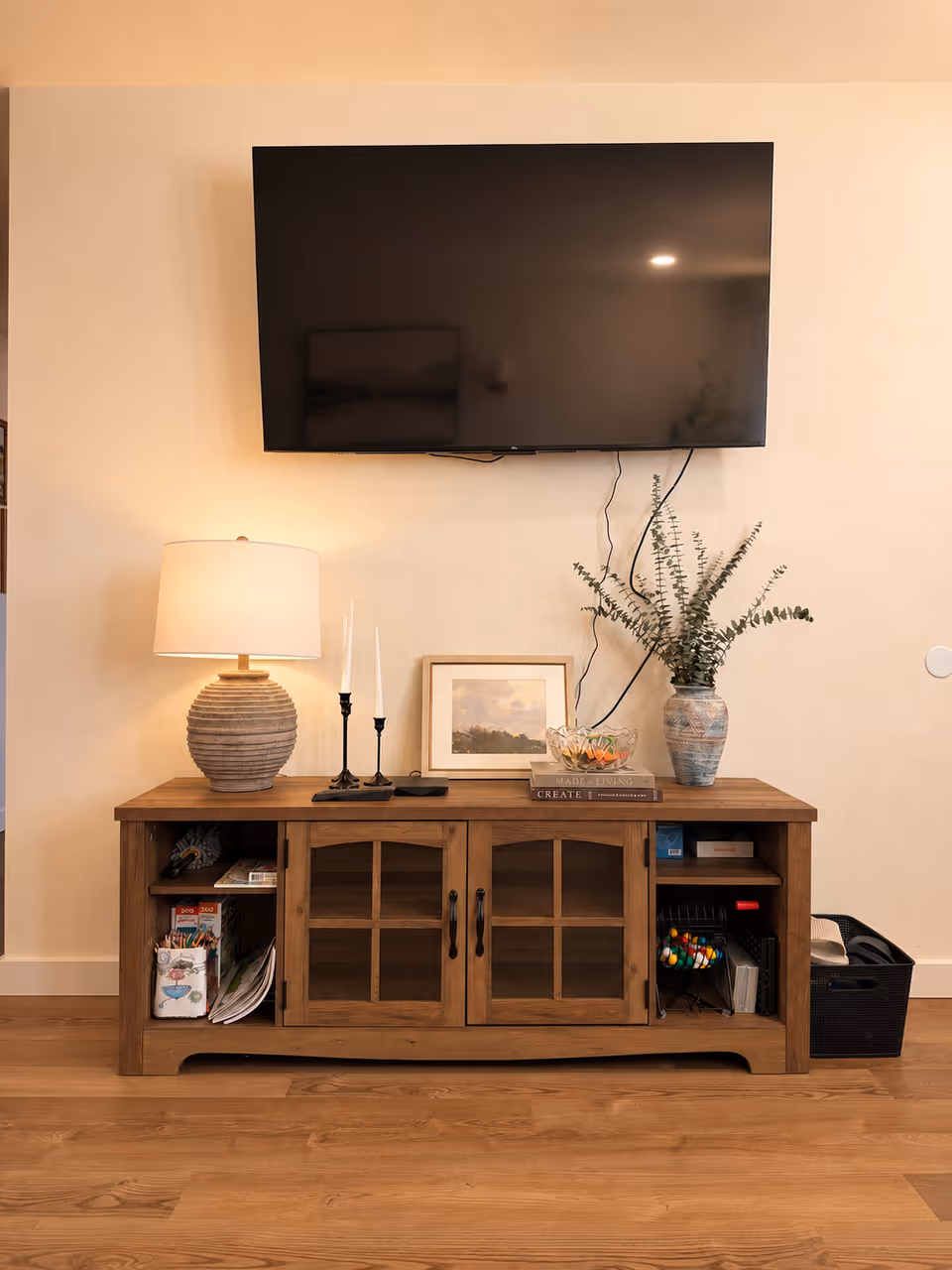 Living room setup with wall-mounted TV, wooden console, lamp, and decorative items.