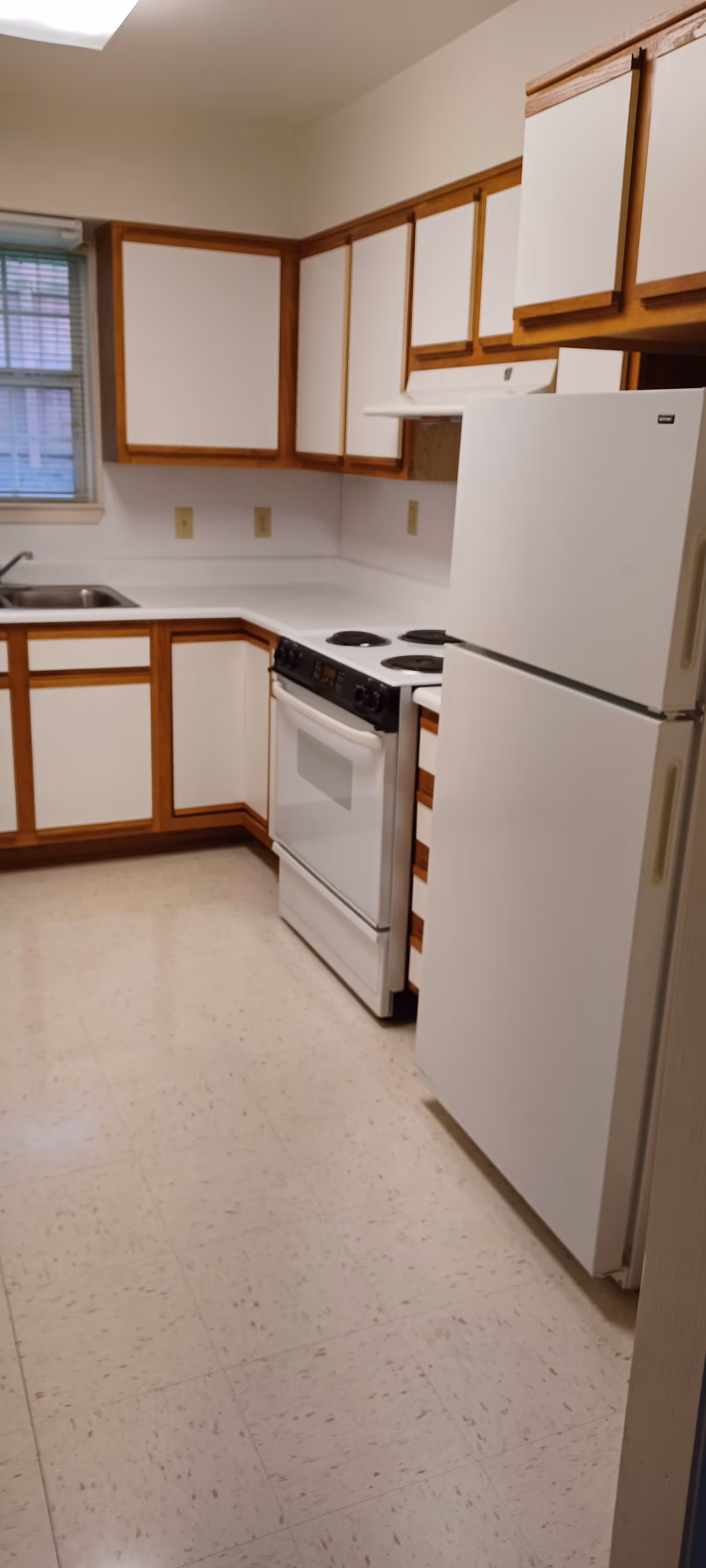 Compact kitchen with white cabinets, stove, and refrigerator in a senior apartment.