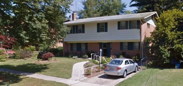 Two-story brick-and-siding senior living building with a driveway, ramp, and parked car.