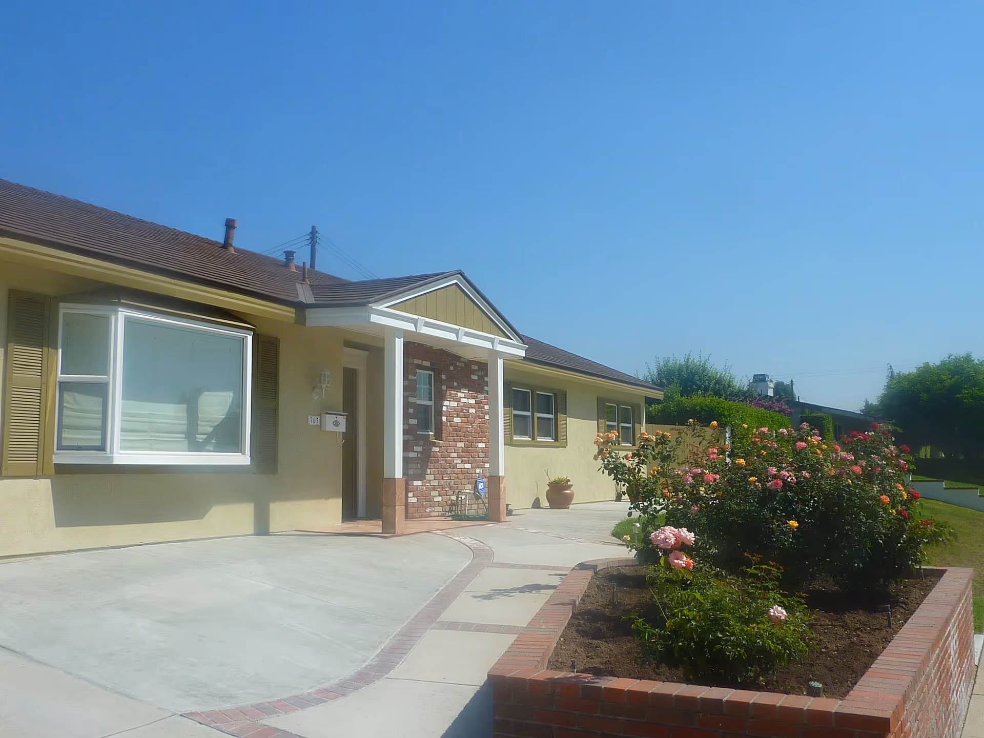 A single-story senior care facility front with brick entry and colorful rose garden.