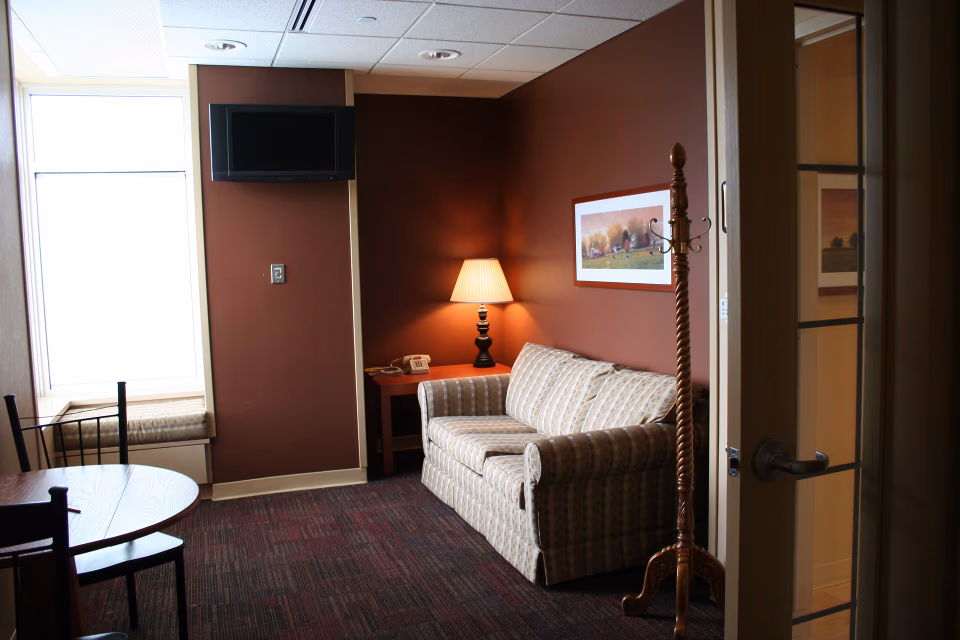 A cozy lounge with sofa, lamp, and artwork in a senior living facility.