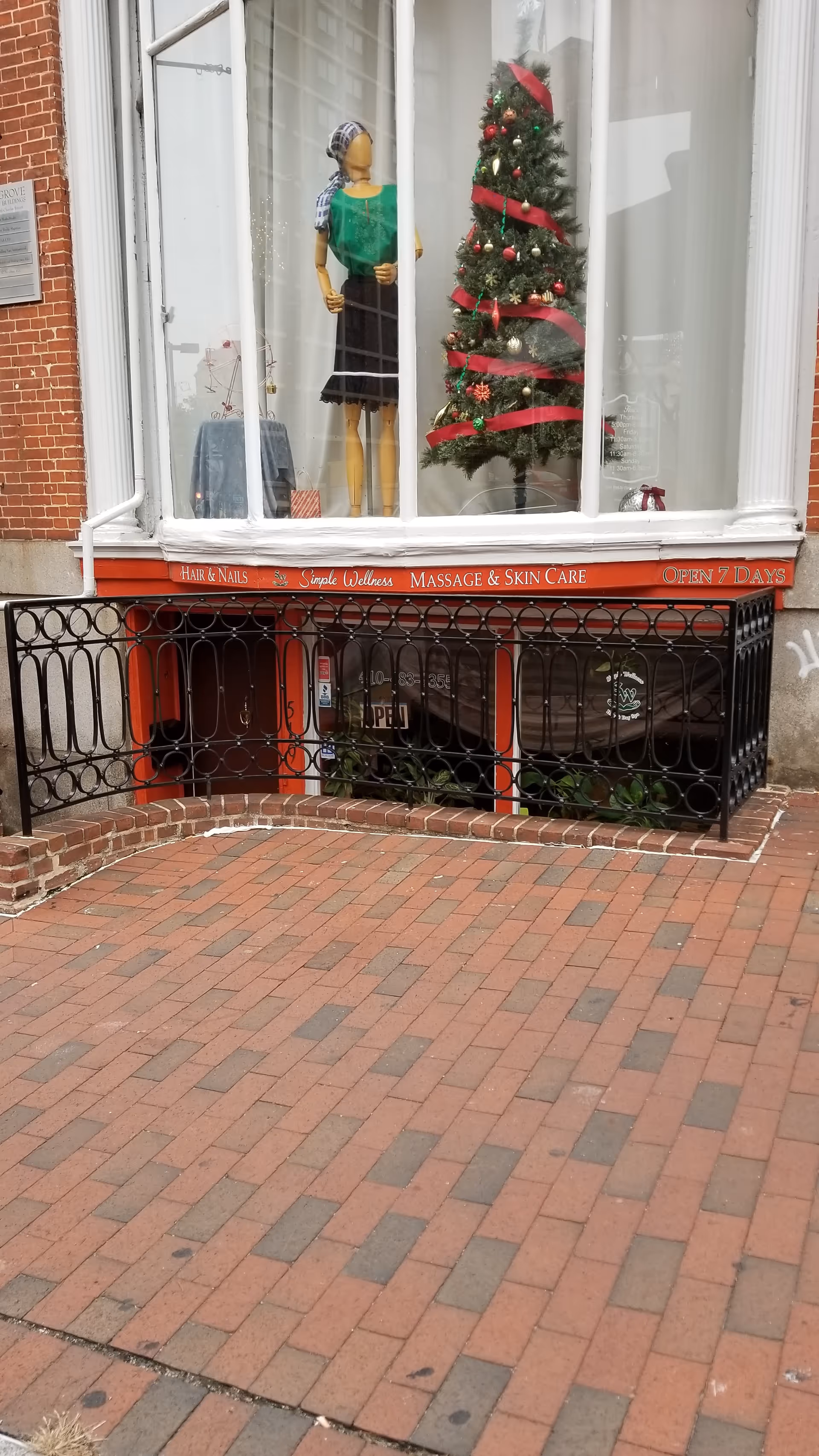 Storefront window with mannequin, Christmas tree, and wrapped gifts on display.