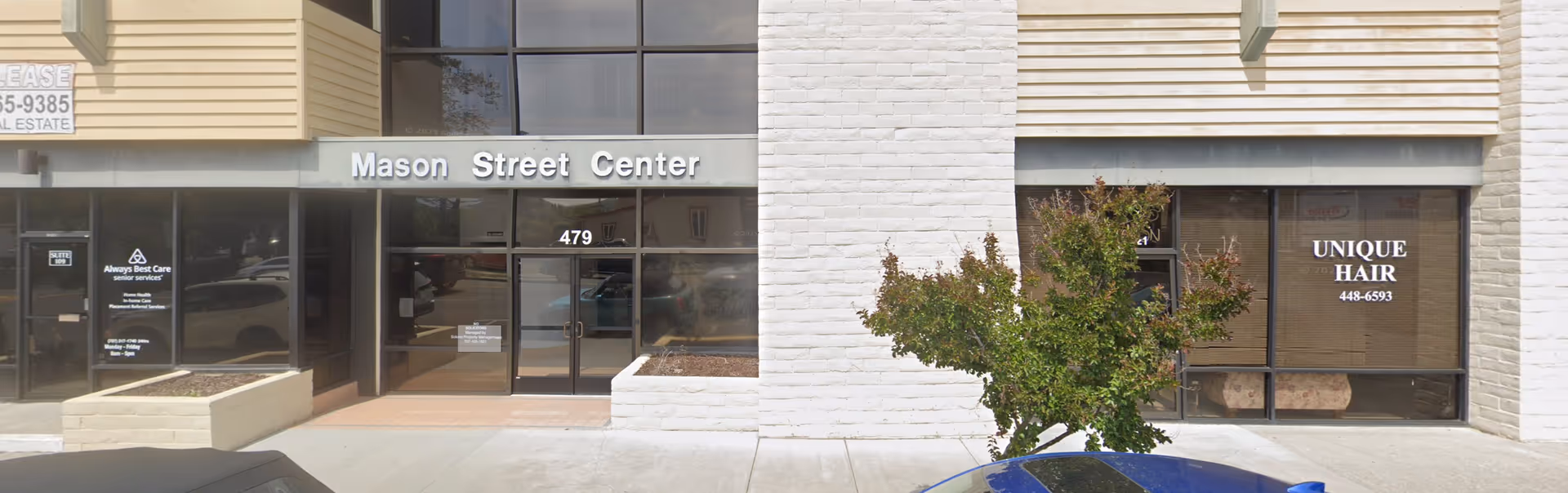 Exterior of Mason Street Center with glass doors, storefronts, and a tree.