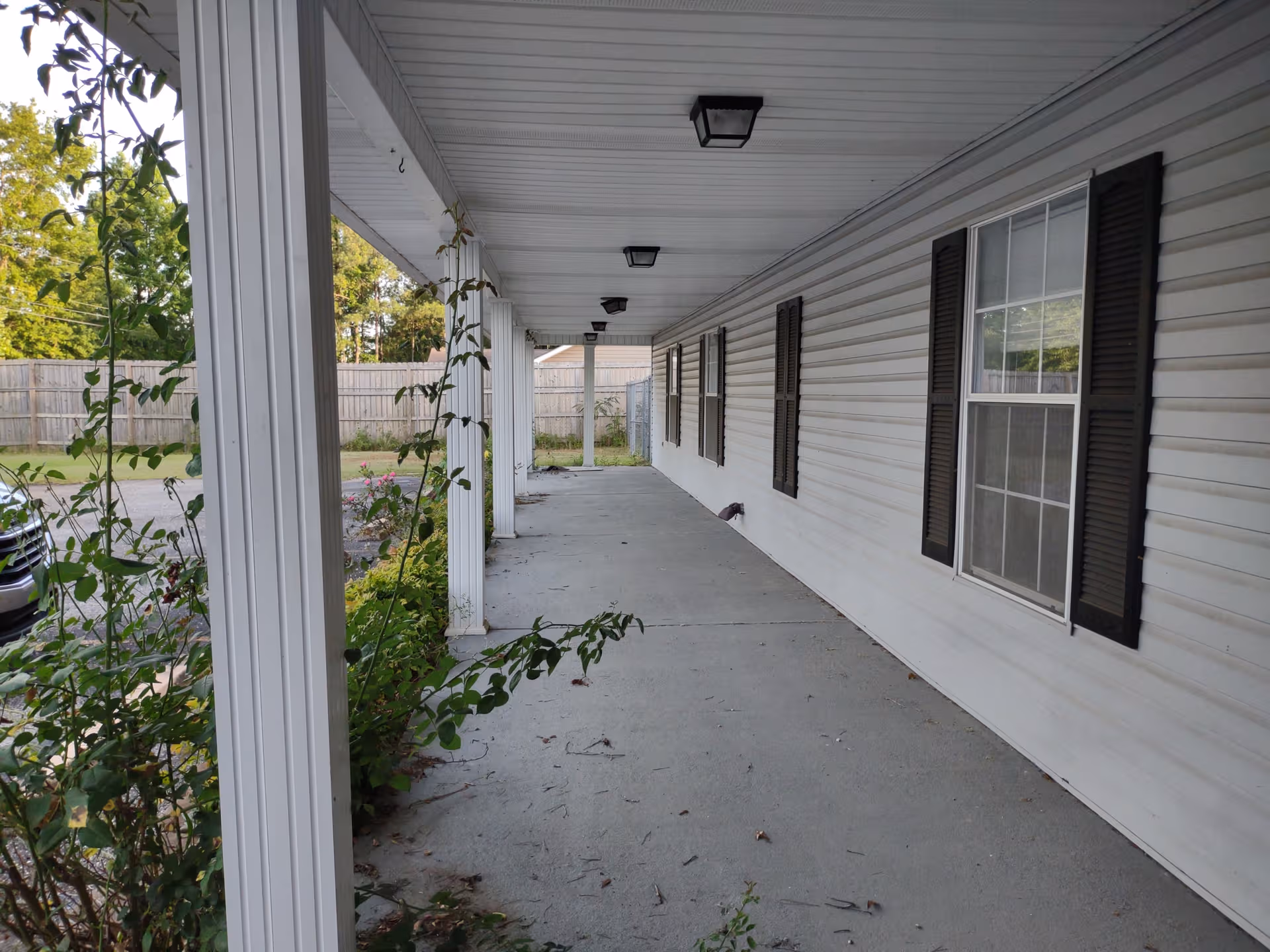 Long covered exterior walkway at Country Oaks Assisted Living with white siding and windows.