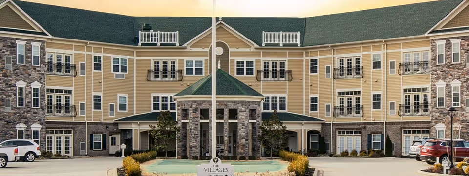 Exterior view of The Villages at the River Club building with entrance and parked cars.