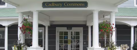 Front entrance of Cadbury Commons with white columns and hanging flower baskets.
