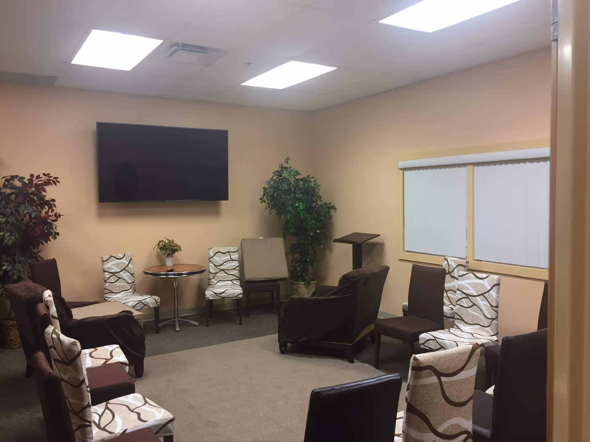 Cozy lounge in a senior living facility with patterned chairs and a wall-mounted TV.