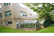 Brick senior living building with glass greenhouse extension and grassy lawn.