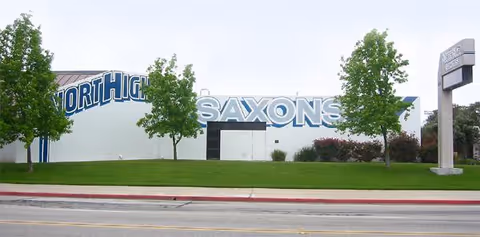 Exterior view of a large light-colored building with blue signage and trees.