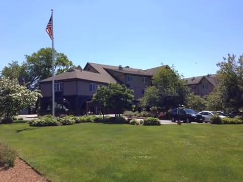 Bertram House of Swampscott exterior with flagpole, manicured lawn, trees, and parked cars.