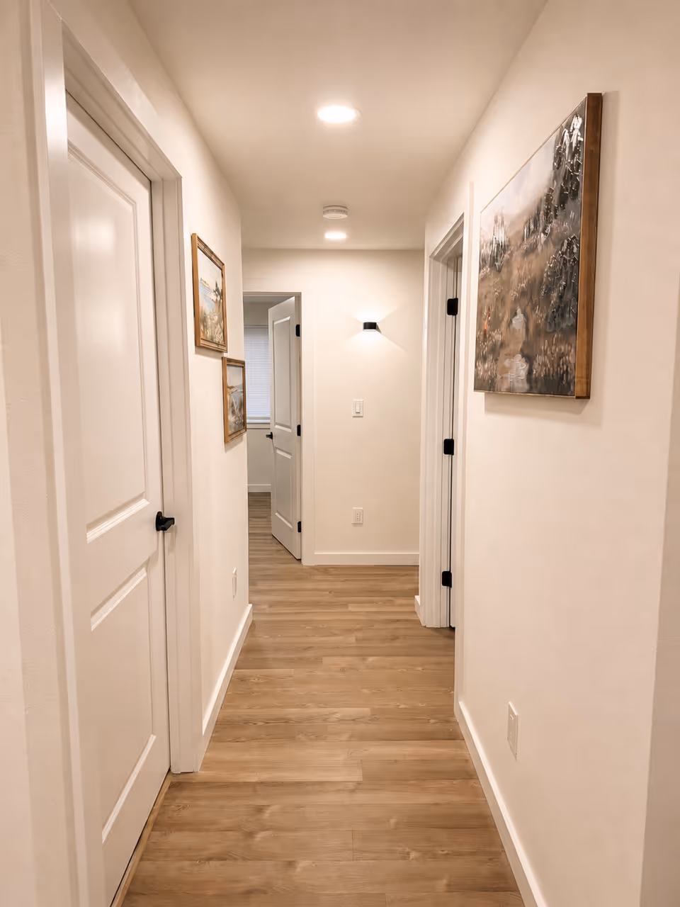 A well-lit hallway in a senior living facility with doors on both sides and wall art.