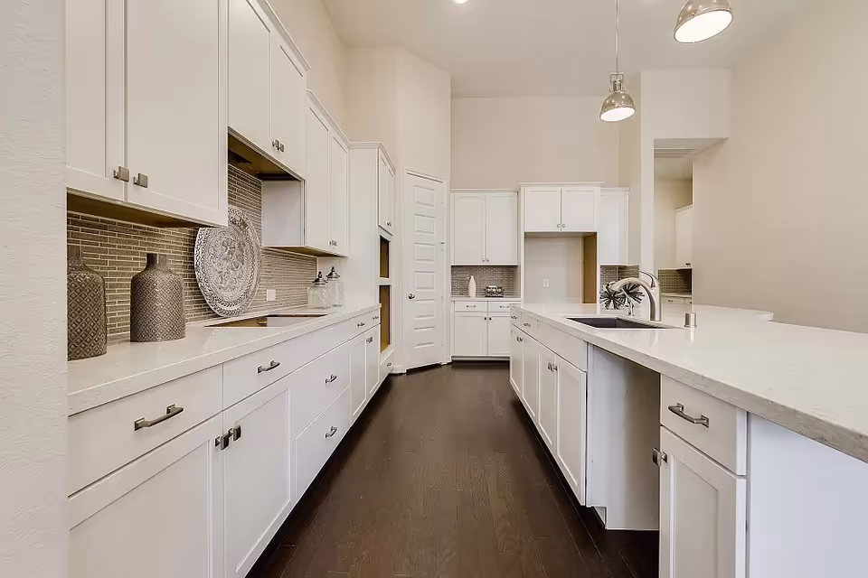 Bright white kitchen with expansive countertops, cabinetry, and dark wood flooring.