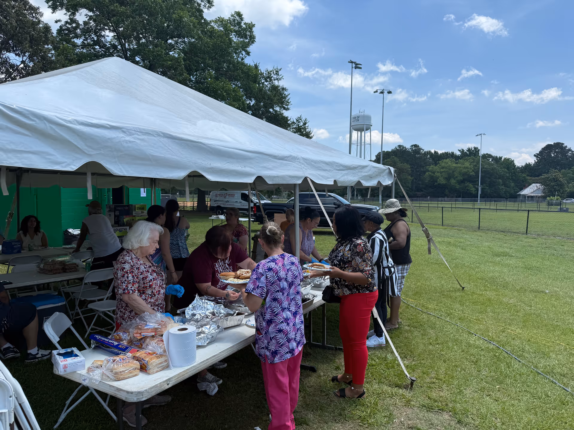 Residents and caregivers line up for food under a white tent at an outdoor event.