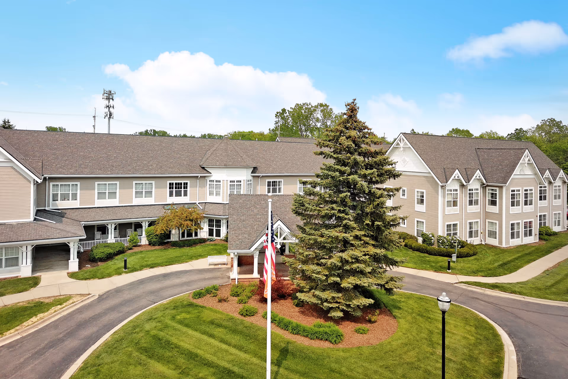 Exterior view of Sunrise of Troy senior living facility with circular drive, flagpole, and landscaped grounds.
