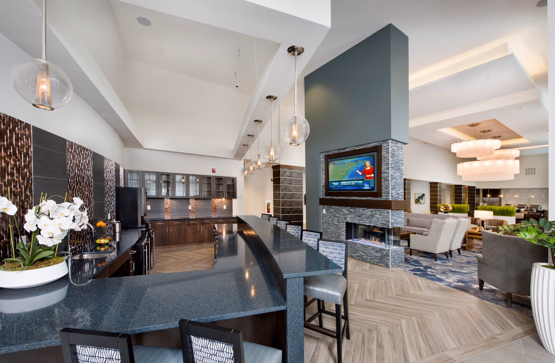 Modern senior living lounge with a long granite bar, seating, fireplace, and TV.
