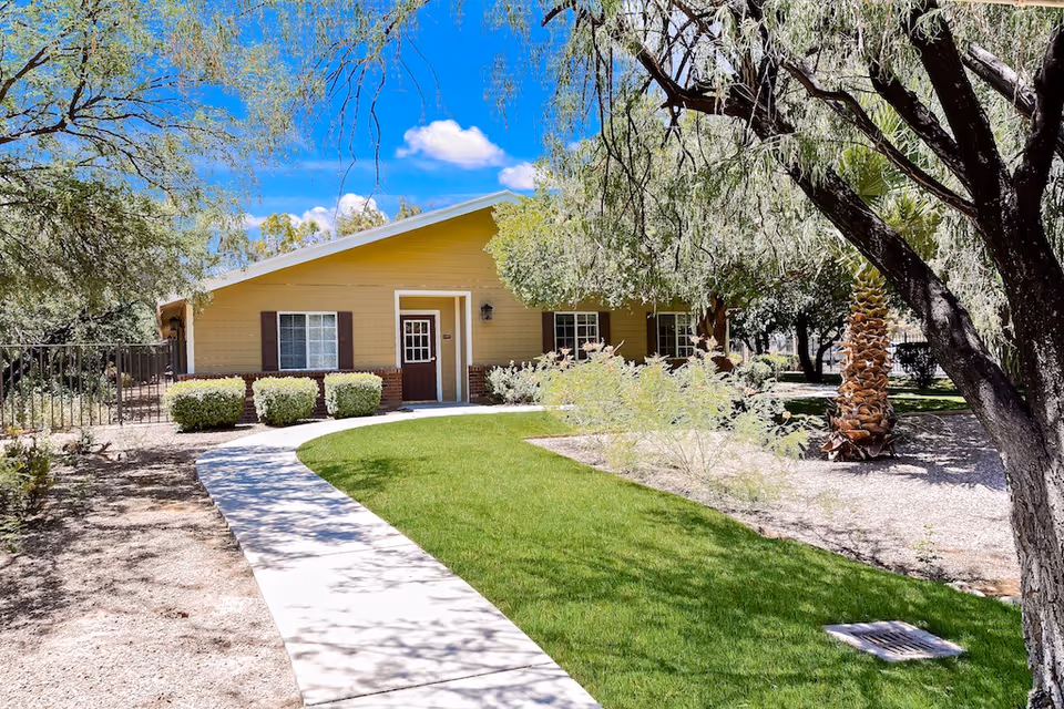 Single-story beige memory care facility with front entrance, green lawn, and curved walkway.