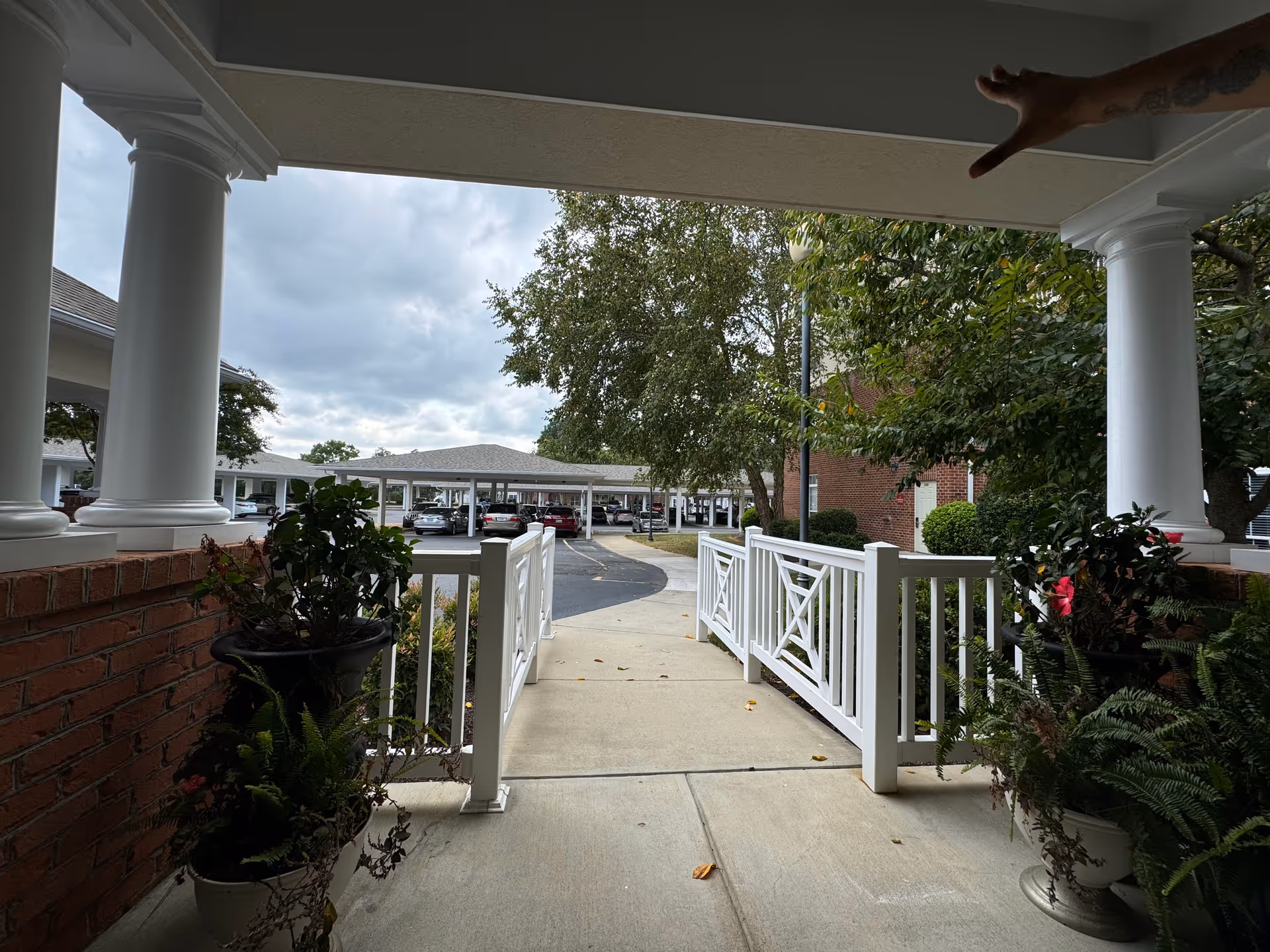 Exterior porch with white columns, railing, and a parking lot beyond.