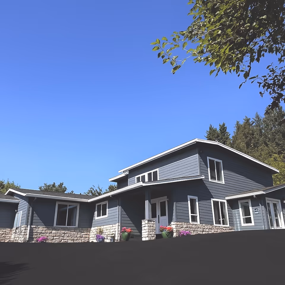 Modern two-story senior living building exterior with blue siding, stone foundation, and potted flowers.