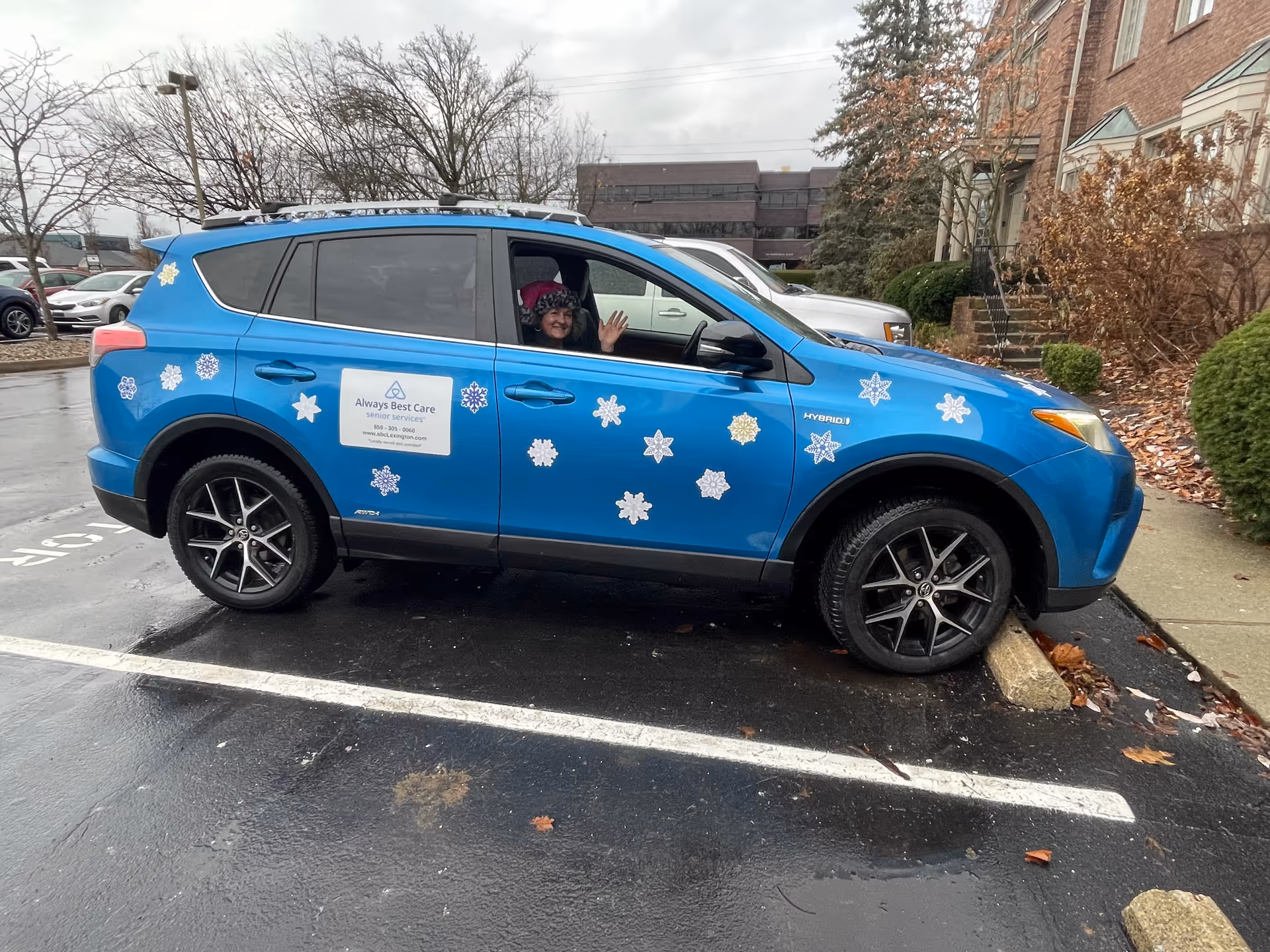 Blue Always Best Care car decorated with snowflakes in a parking lot; driver waves.