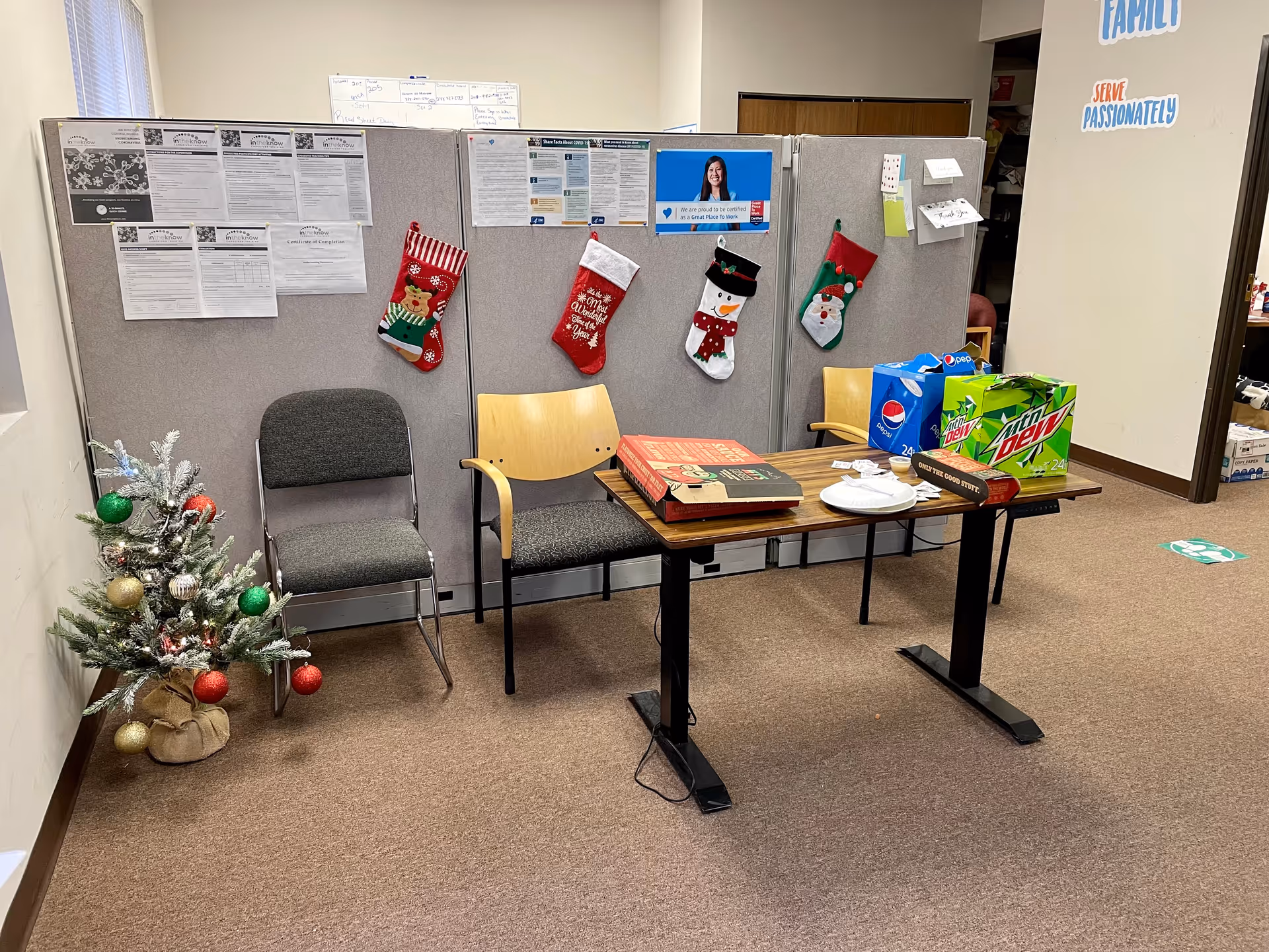 A small office area with a partition, Christmas stockings, a Christmas tree, chairs, and a table.