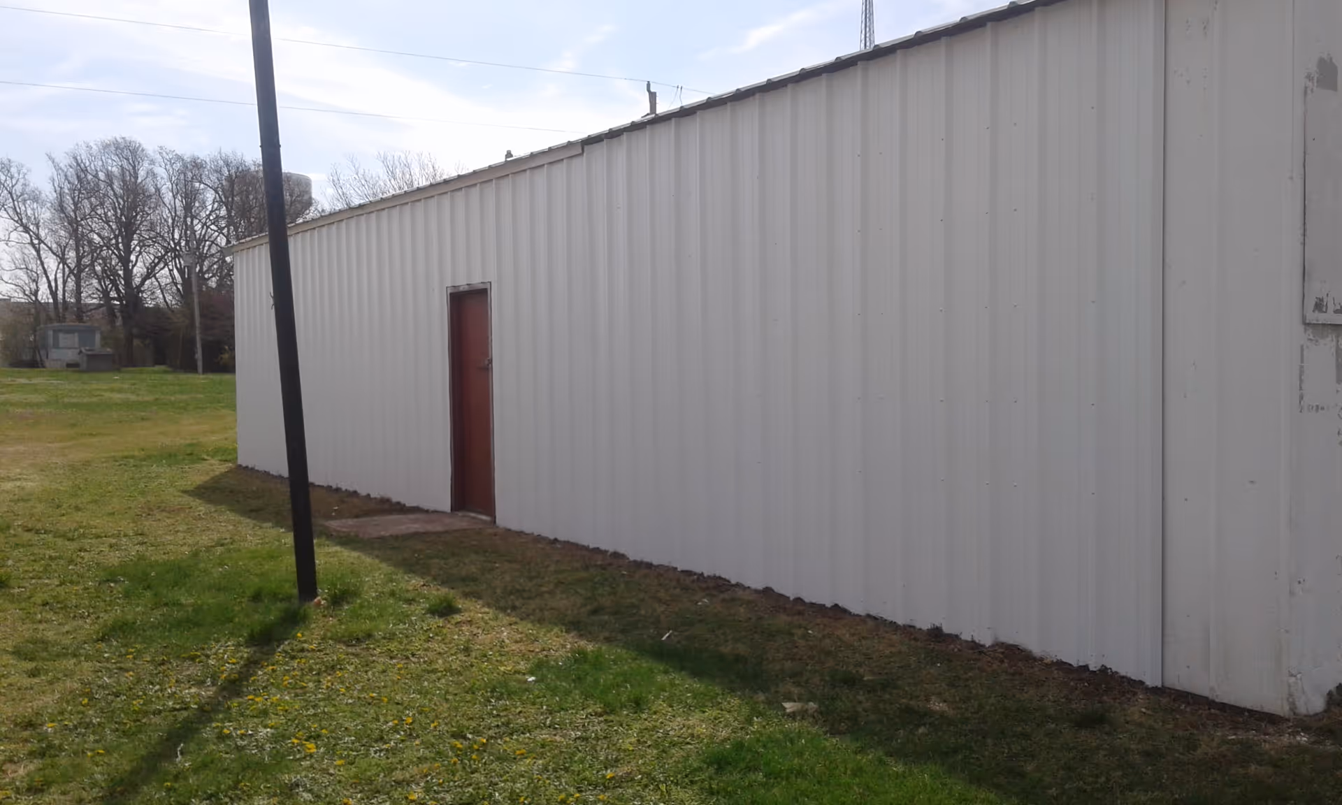 A long white metal building exterior with a red door and grassy foreground.