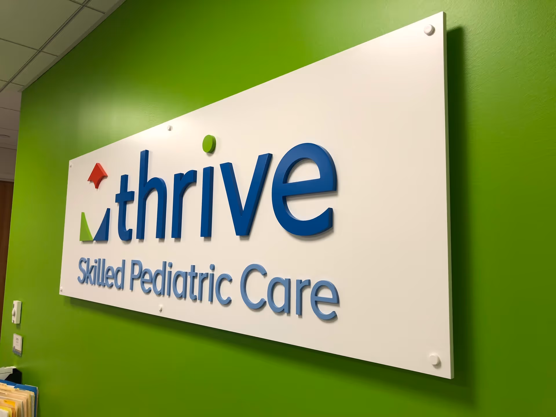 Thrive Skilled Pediatric Care sign mounted on a bright green interior wall.