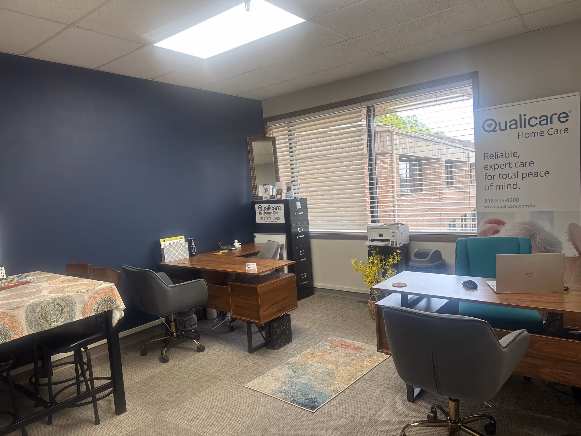 Interior office space with desks, chairs, a banner, and blinds at Qualicare Home Care Kansas City.