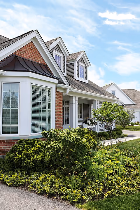 A single-story senior living facility exterior with brick facade, gabled dormers, and landscaped front yard.
