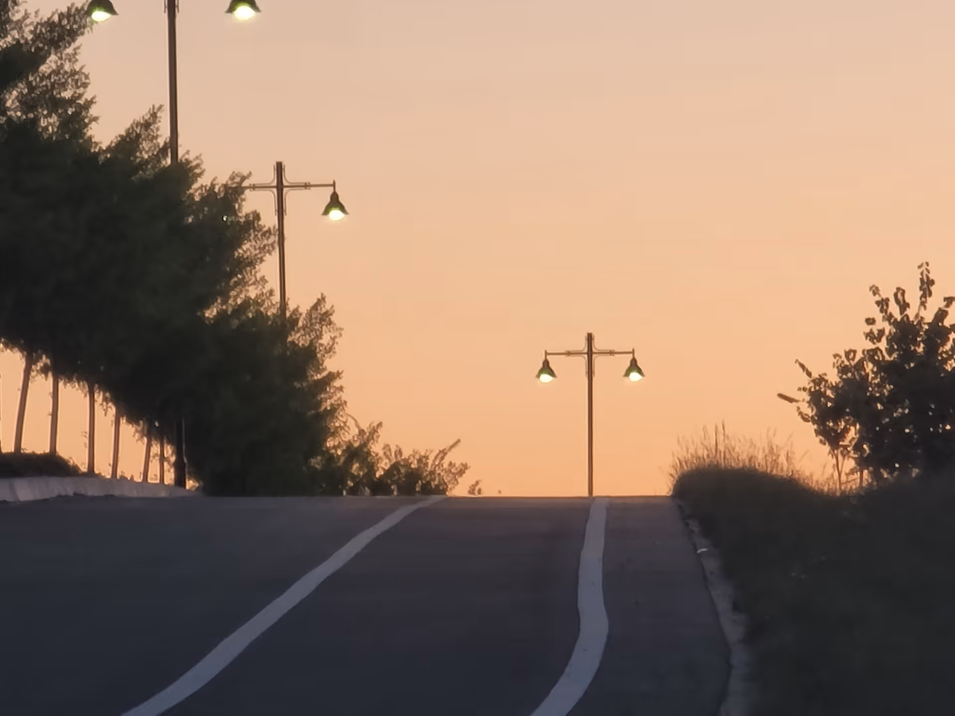 Sunset-lit road with street lamps and trees along a gentle incline.