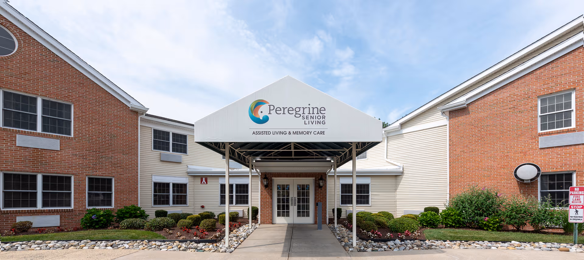 Front entrance of Peregrine Senior Living building with brick wings and canopy.