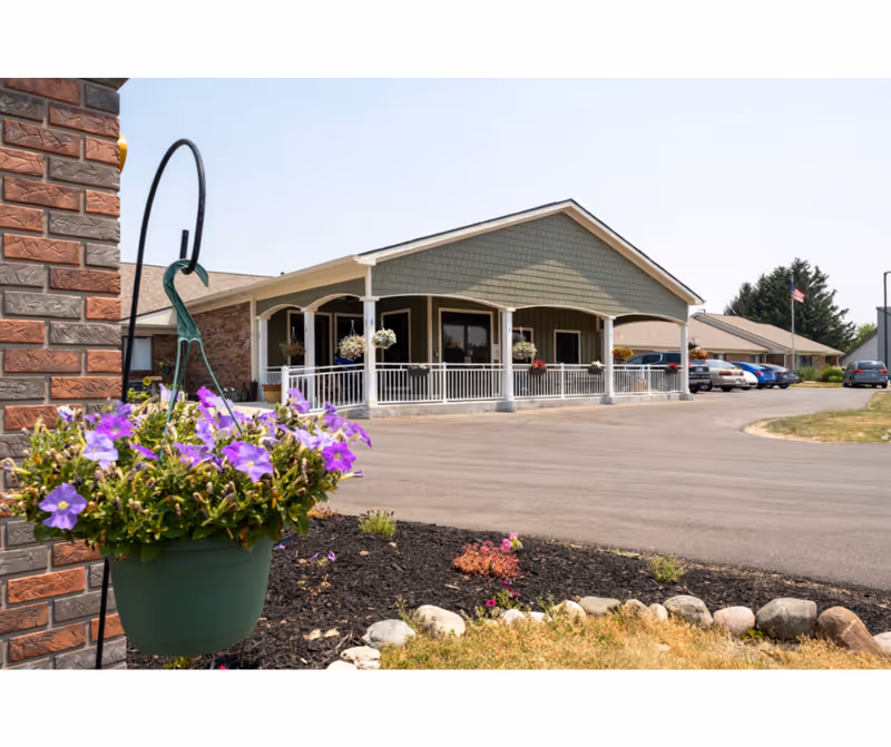 Exterior view of a senior care center with a wraparound porch and hanging planters.