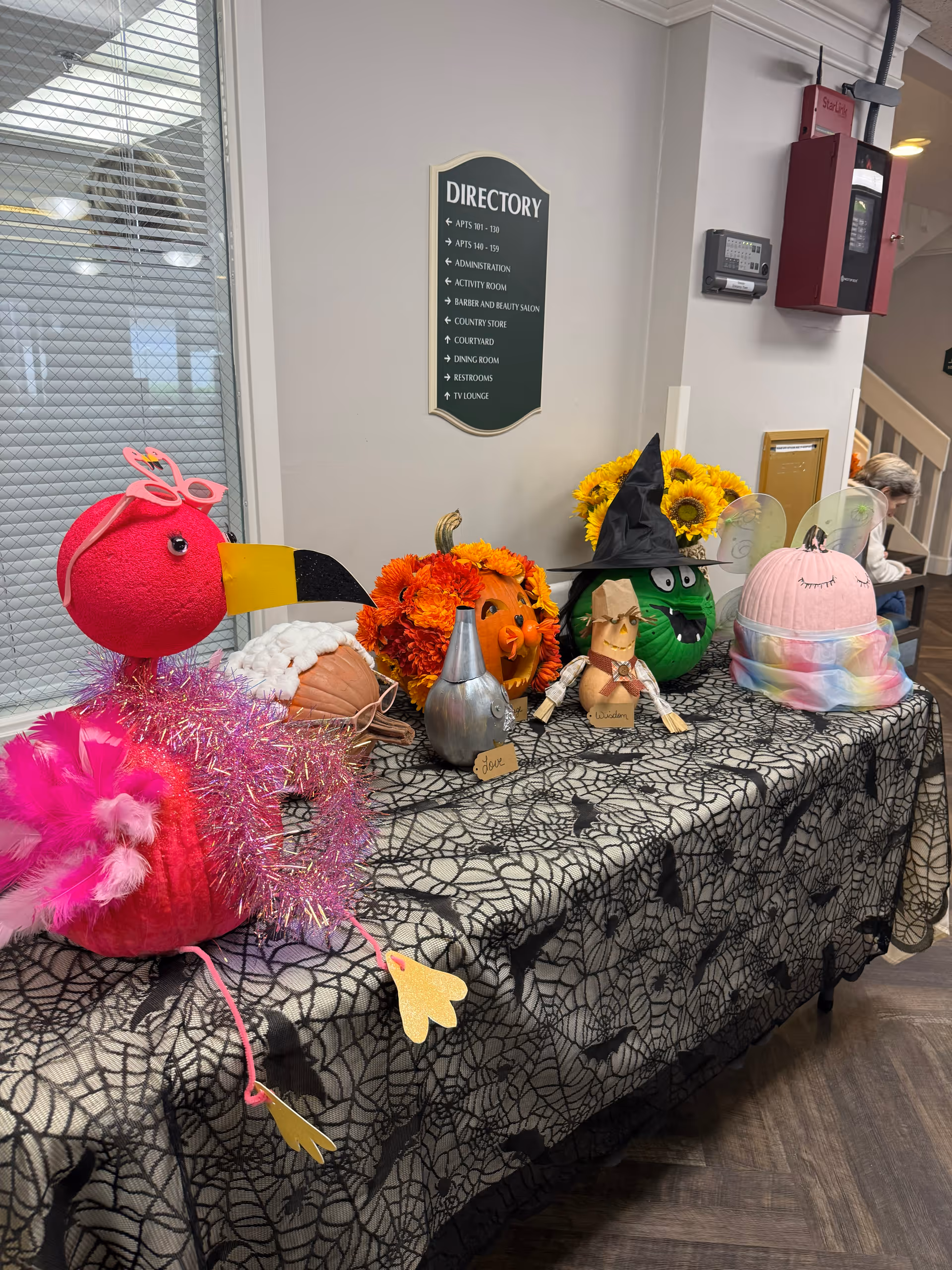 Table of decorative pumpkins and crafts arranged on a patterned table inside a senior facility.