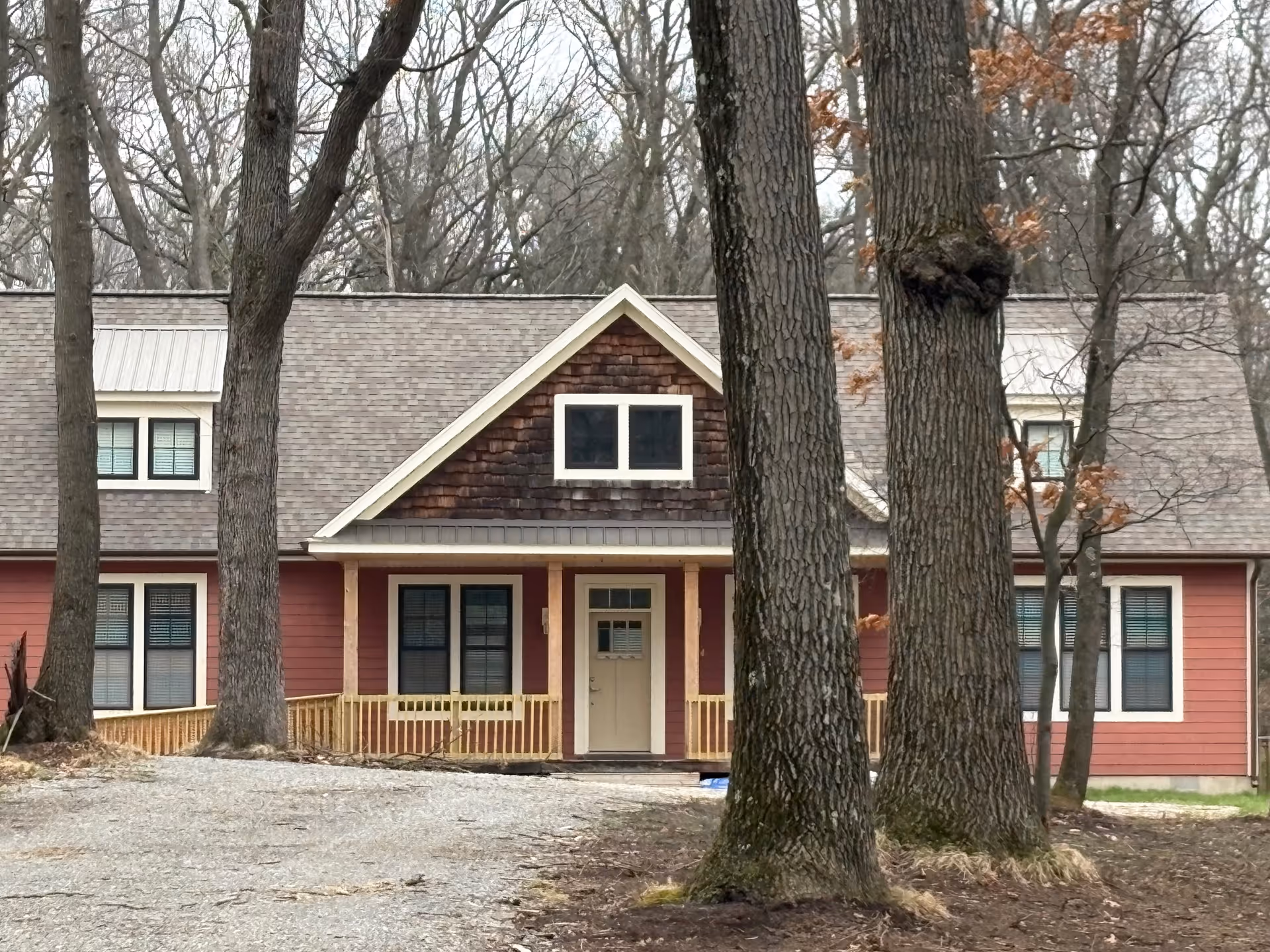 A red senior living facility building with a porch and tall trees in front.