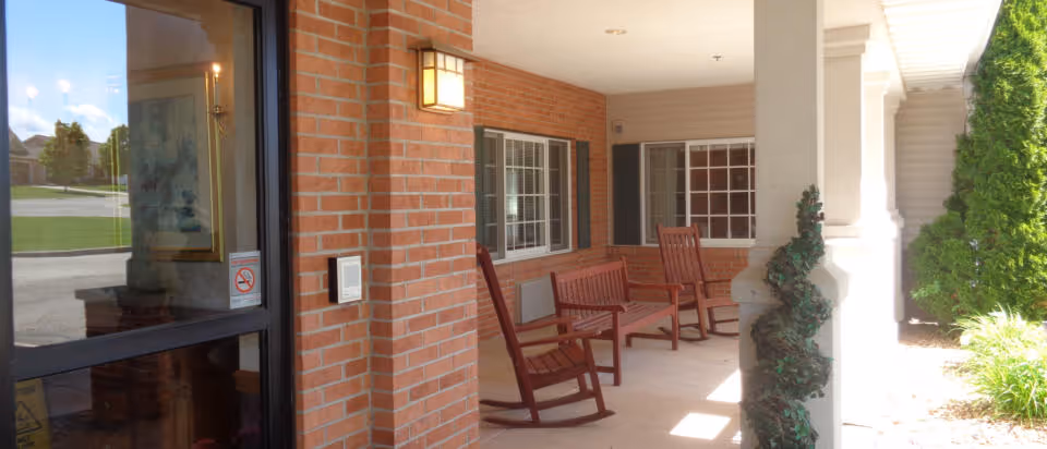 Covered front porch with brick walls, a glass entry door and several wooden rocking chairs.