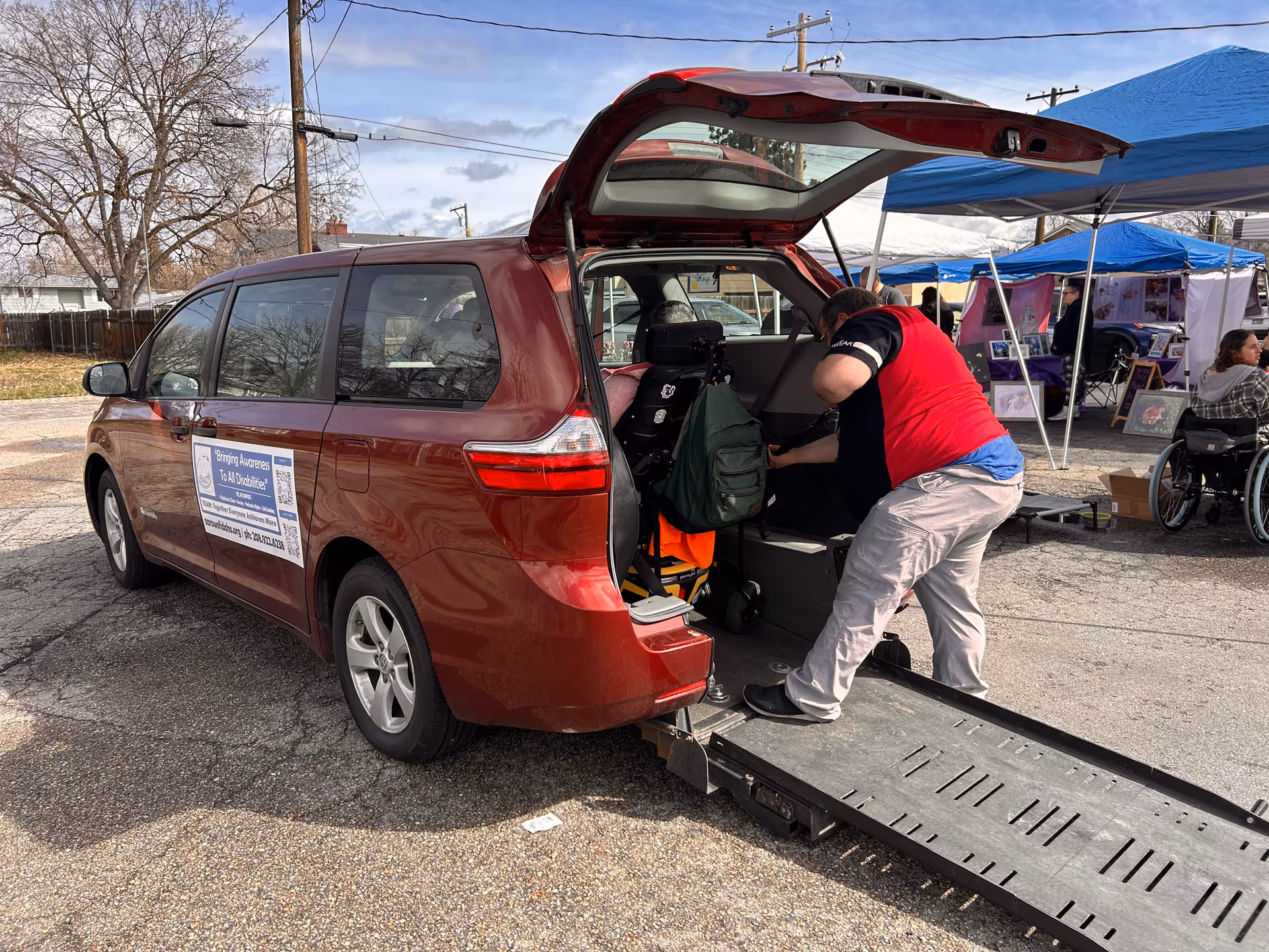 Red minivan with ramp extended; caregiver assists a resident outdoors.