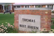 Brick sign reading Thomas Rest Haven with grassy lawn and building in background.