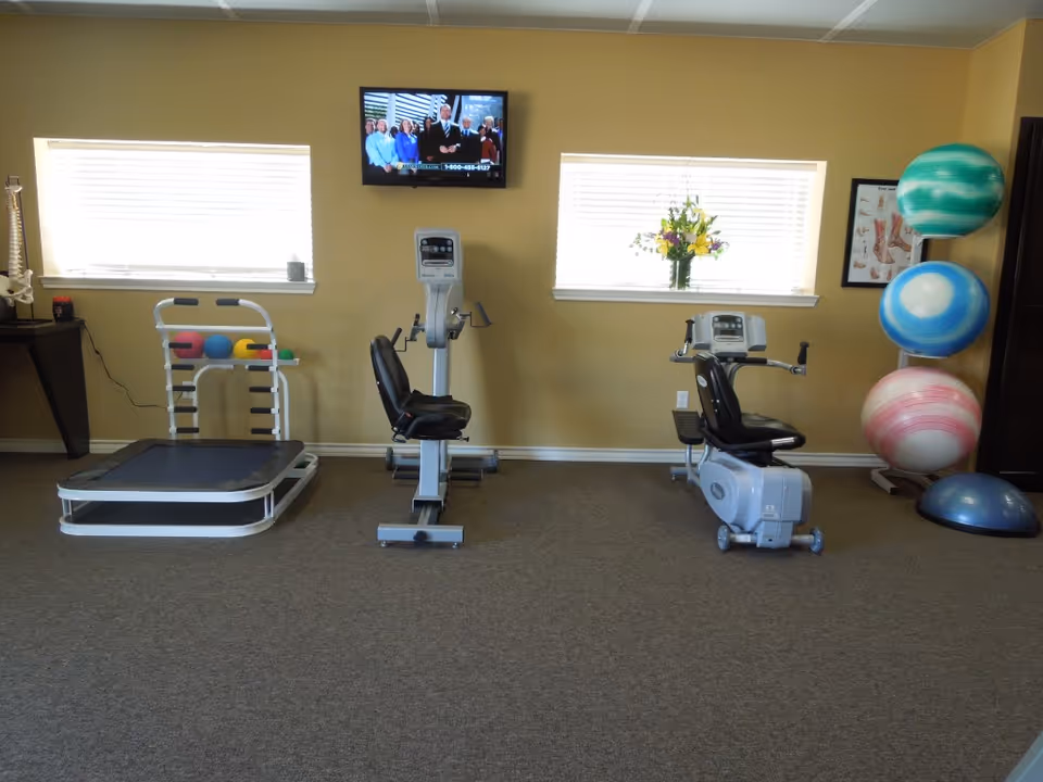 Interior fitness room with exercise bikes, a treadmill, balls, and a TV.