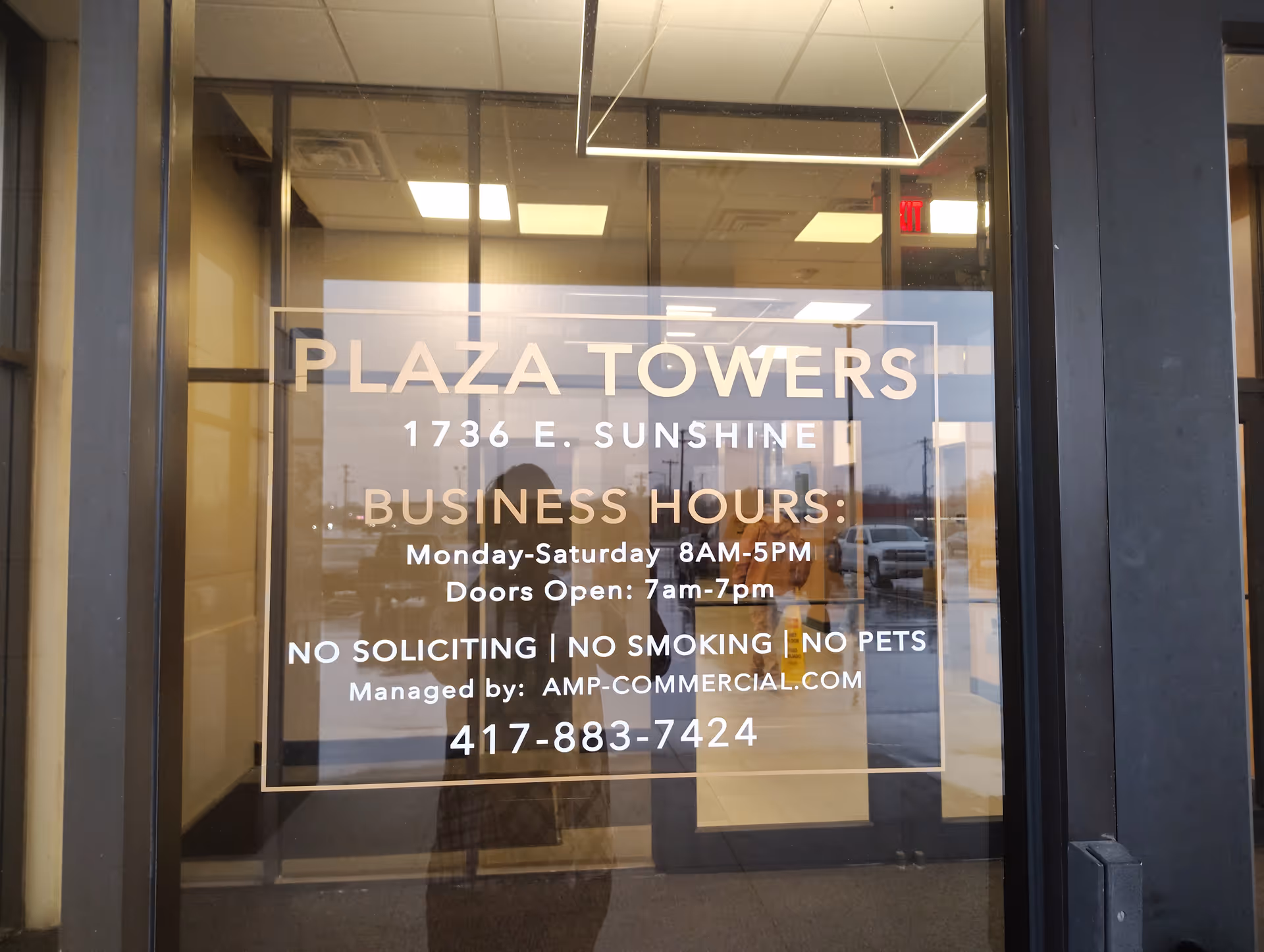 Glass storefront door displaying Plaza Towers sign and business hours.